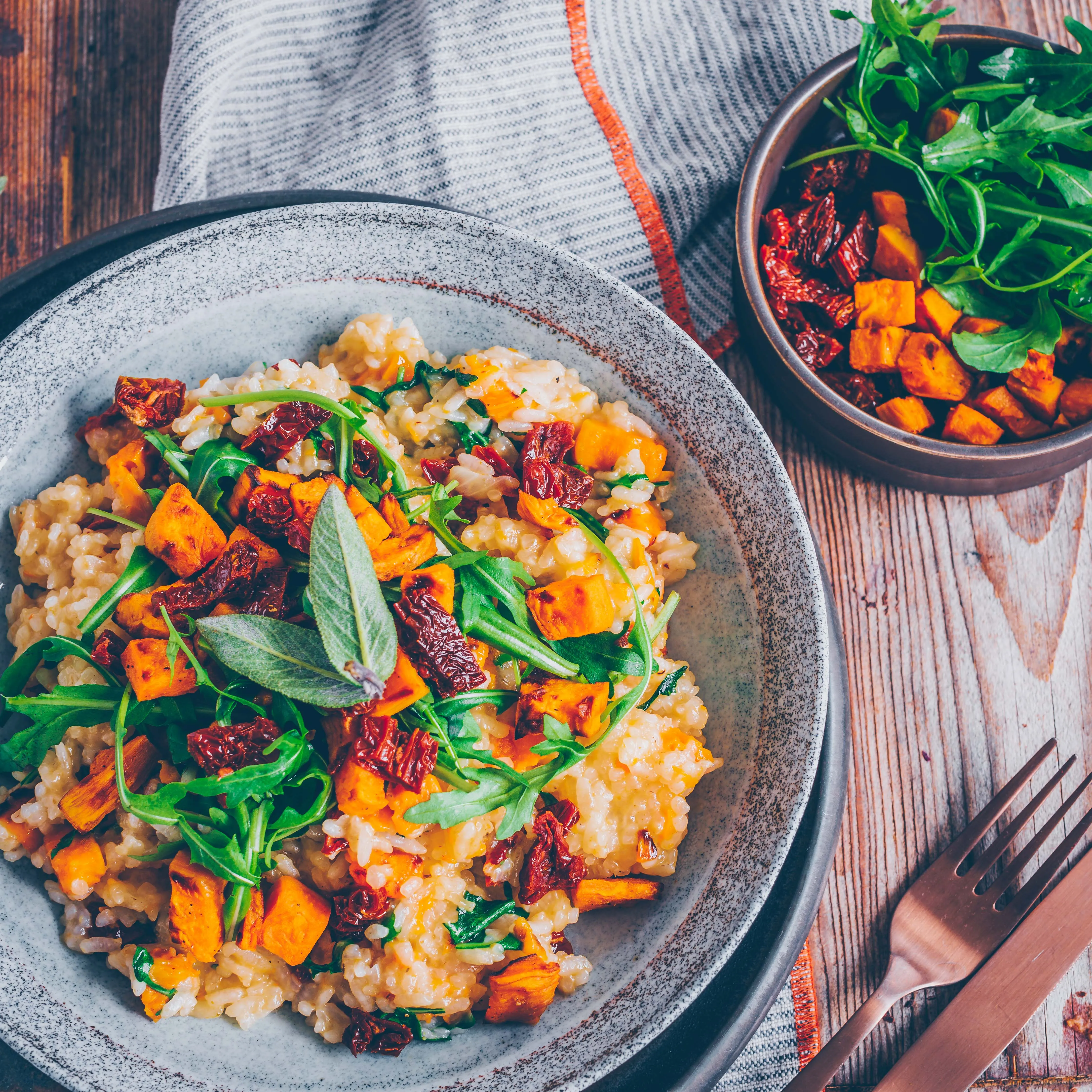 Cremiges Süßkartoffel-Risotto mit getrockneten Tomaten und Rucola in einer Schale angerichtet