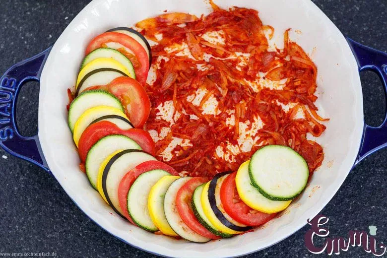 Dachziegelartig geschichtetes Gemüse (Zucchini, Aubergine, Tomate) auf der Tomatenbasis in einer runden Auflaufform.