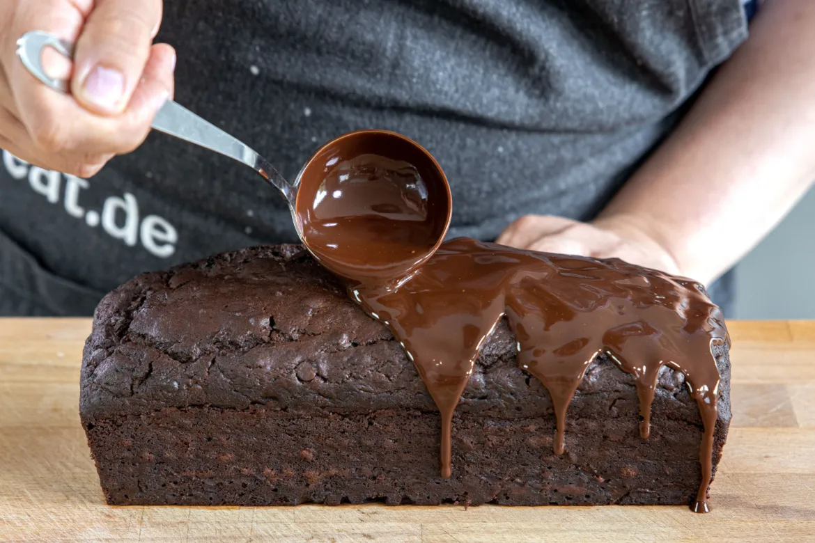 Das Auftragen einer Schokoladenglasur auf einen Kuchen, um ihn zu konservieren und saftig zu halten, ideal beim Kuchenversand