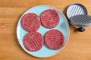 Das Formen eines runden Burger-Pattys aus Hackfleisch mithilfe einer Burgerpresse, um eine gleichmäßige Form zu gewährleisten.