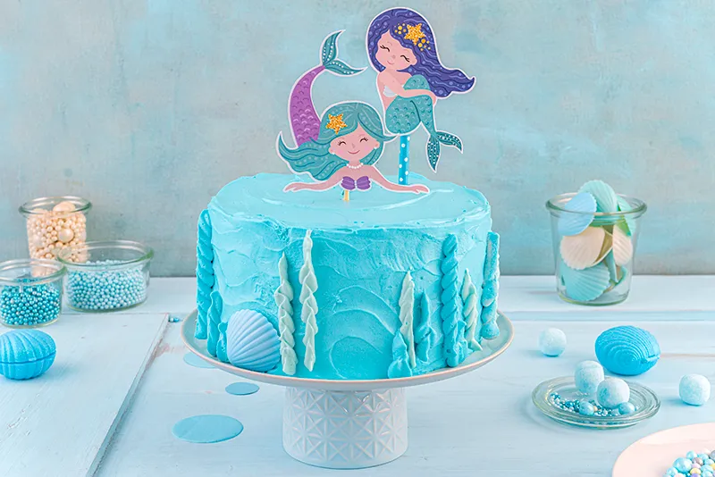 Das kunstvolle Spritzen von Korallen und Unterwasserpflanzen mit verschiedenfarbiger Schlagcreme an den Seiten der Meerjungfrauen Torte.