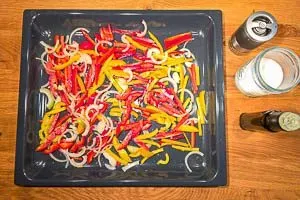 Das vorbereitete und gewürzte Gemüse, bestehend aus Paprika, Zwiebeln und Peperoni, wird gleichmäßig auf einem Backblech verteilt