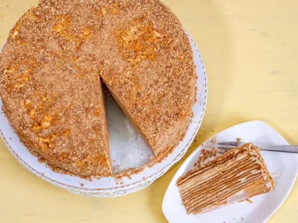 Der fertige russische Kuchen, Medovik, als ganze Torte, umhüllt von einer feinen Schicht aus zerbröselten Teigresten, bereit zum Servieren.