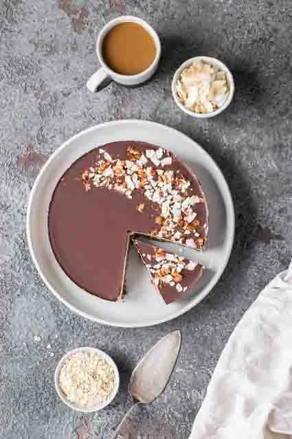 Der gesamte vegane glutenfreie Kuchen mit Schokoladenglasur und Kokosraspeln, bereit zum Anschneiden.