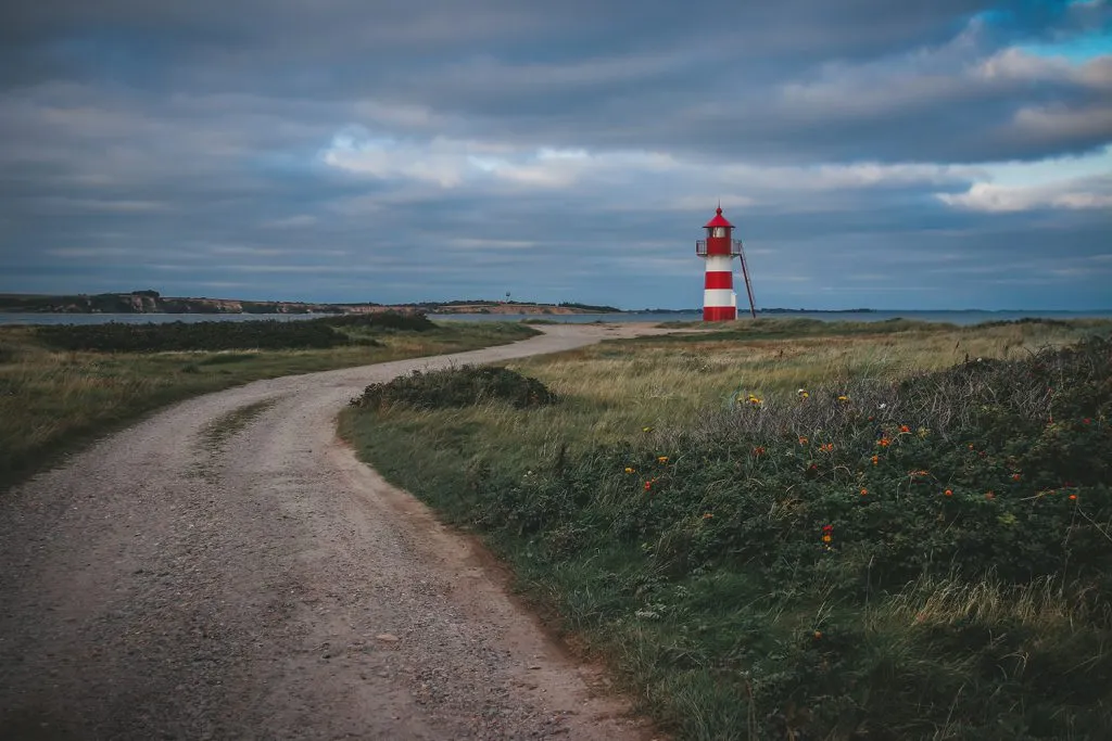 Der Grisetå Odde Fyr, ein kleiner roter Leuchtturm an der Küste, umgeben von ruhigem Wasser und sanftem Licht