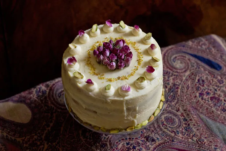 Detailaufnahme einer luxuriösen Pistazien-Rosen-Torte mit fein gearbeiteten Tupfen und essbaren Blütenblättern