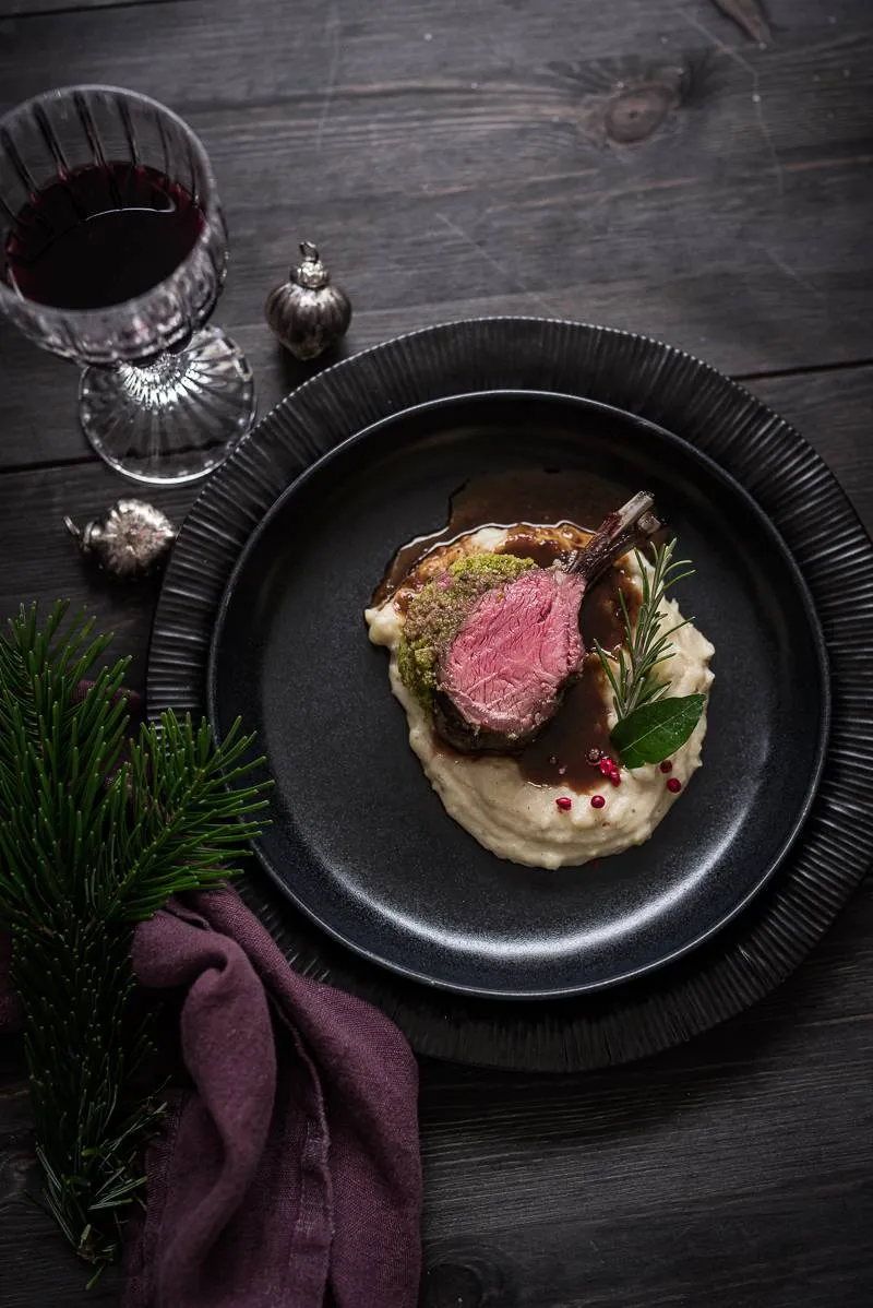 Detailaufnahme eines Tellers mit Lammkarree, das die Kruste, den Querschnitt des Fleisches und den Jus hervorhebt.