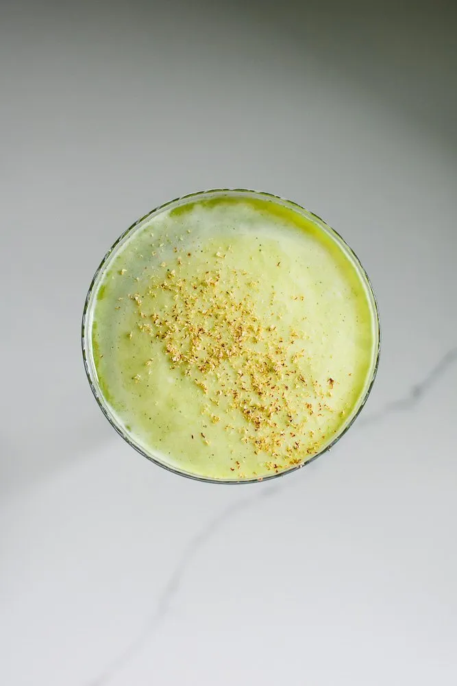 Die cremige obere Schicht eines Matcha-Martinis mit Stücken frischer Muskatnuss, die darauf schwimmen.