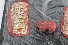 Die gefüllte Roulade wird mit Küchengarn sorgfältig zu einem Päckchen gebunden, um die Füllung beim Schmoren zu halten.