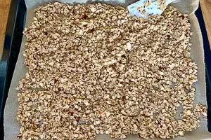 Die Granola-Mischung wird gleichmäßig auf einem mit Backpapier ausgelegten Backblech verteilt, bereit zum Backen.