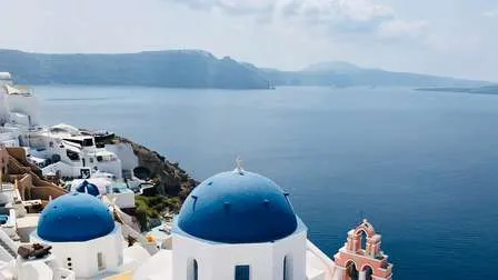 Die ikonischen blauen Kuppeldächer der Kirchen in Oia, Santorin, vor dem weißen Kykladen-Häusern und dem Ägäischen Meer.