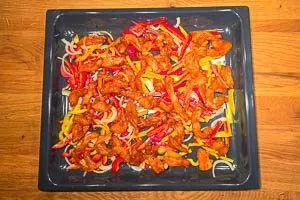 Die marinierten Hähnchenbruststreifen werden auf dem Backblech über das bunte Gemüse gegeben, bereit für den Ofen