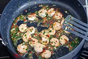 Die Olivenöl-Kräuter-Mischung zu den angebratenen Garnelen in die Pfanne geben und kurz anrösten, um die Aromen perfekt zu verbinden, eine beliebte Technik in der schnellen Küche.