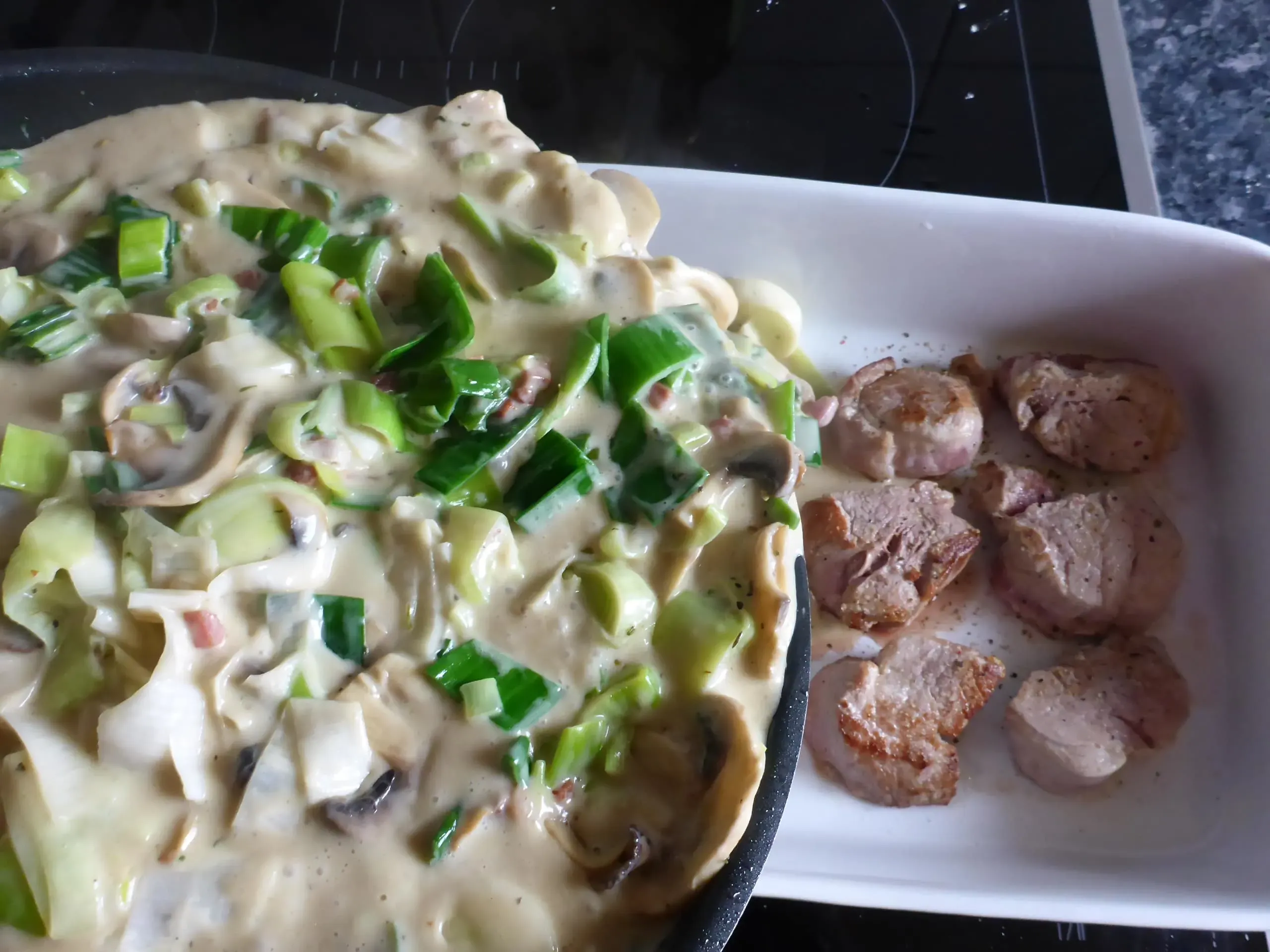 Die reichhaltige Lauch-Pilz-Rahmsauce mit Speck wird gleichmäßig über die angebratenen Schweinefilet-Medaillons in der Auflaufform gegossen, der nächste Schritt zur perfekten Schnitzelpfanne.