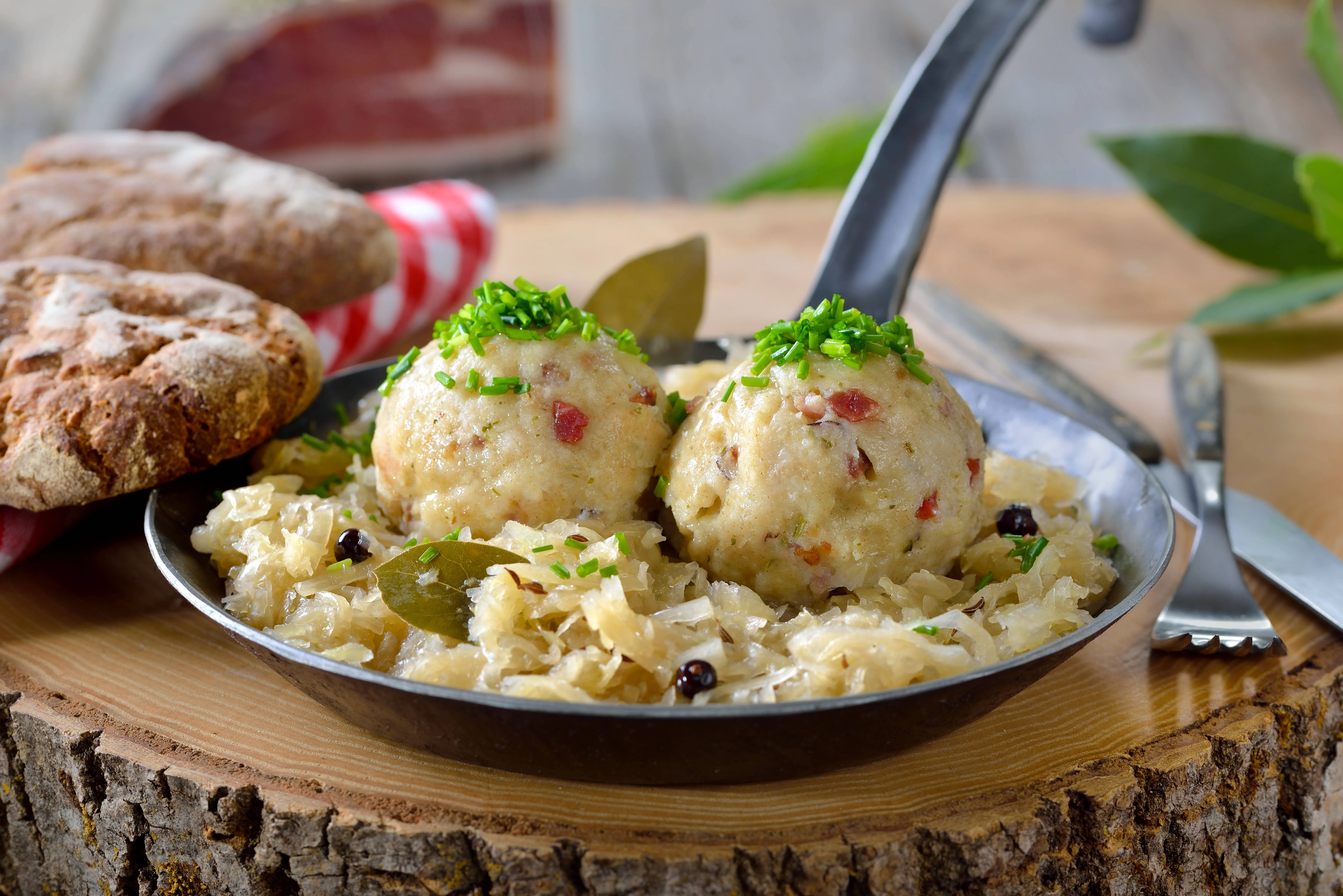 Drei dampfende Südtiroler Speckknödel, garniert mit frischer Petersilie und Parmesan, serviert in einer klaren Brühe.
