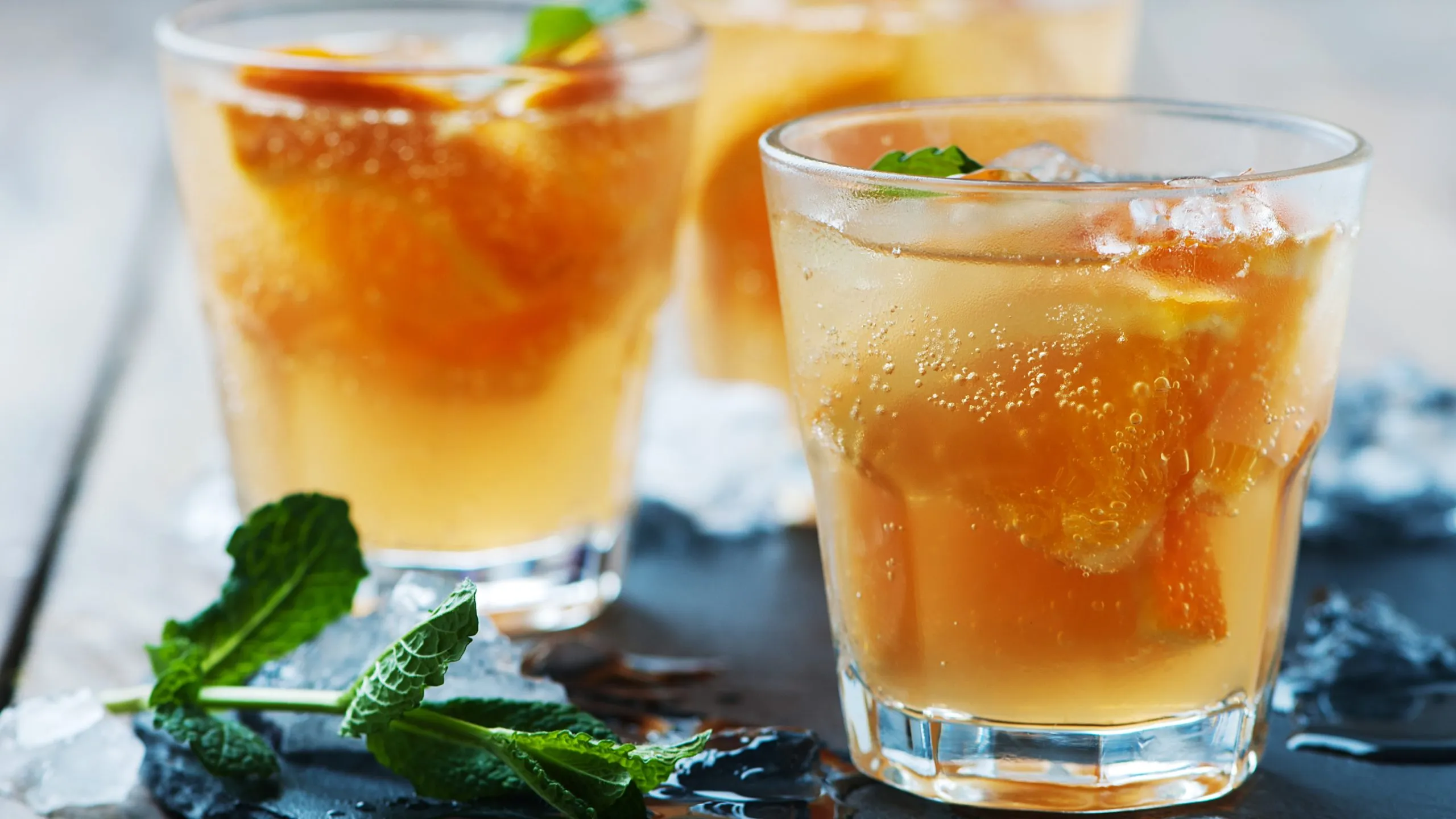 Drei Gläser Lillet Orange Spritz auf einem Holztisch mit Minze und Orangenscheiben