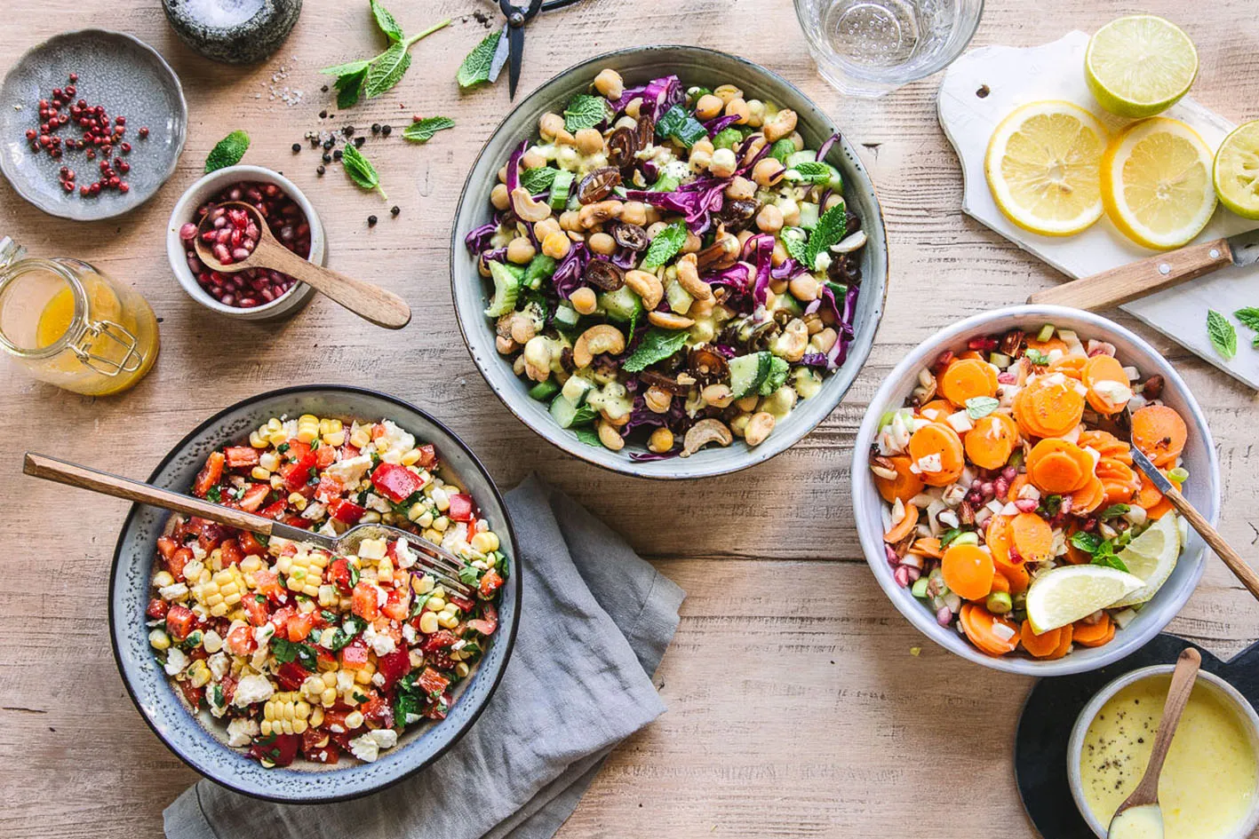 Drei Grillsalate in Schüsseln mit Zutaten auf Holztisch