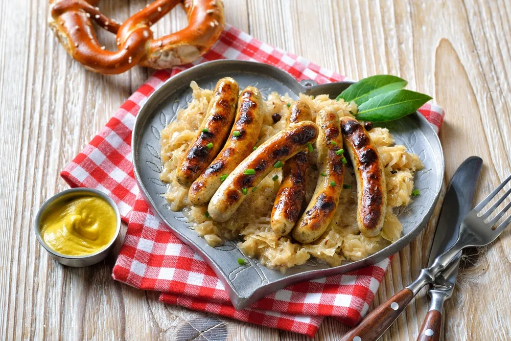 Drei Nürnberger Rostbratwürste auf Sauerkraut mit frischen Kräutern in einem Topf