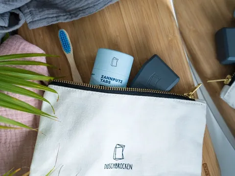 Duschbrocken Reise-Set mit Zahnbürste, fester Zahnpaste und mini FAIRpackung auf Holz liegend