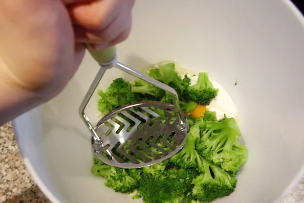 Ei, Mehl, Parmesan und Knoblauch werden in einer weißen Schüssel für die Brokkoli-Puffer vorbereitet