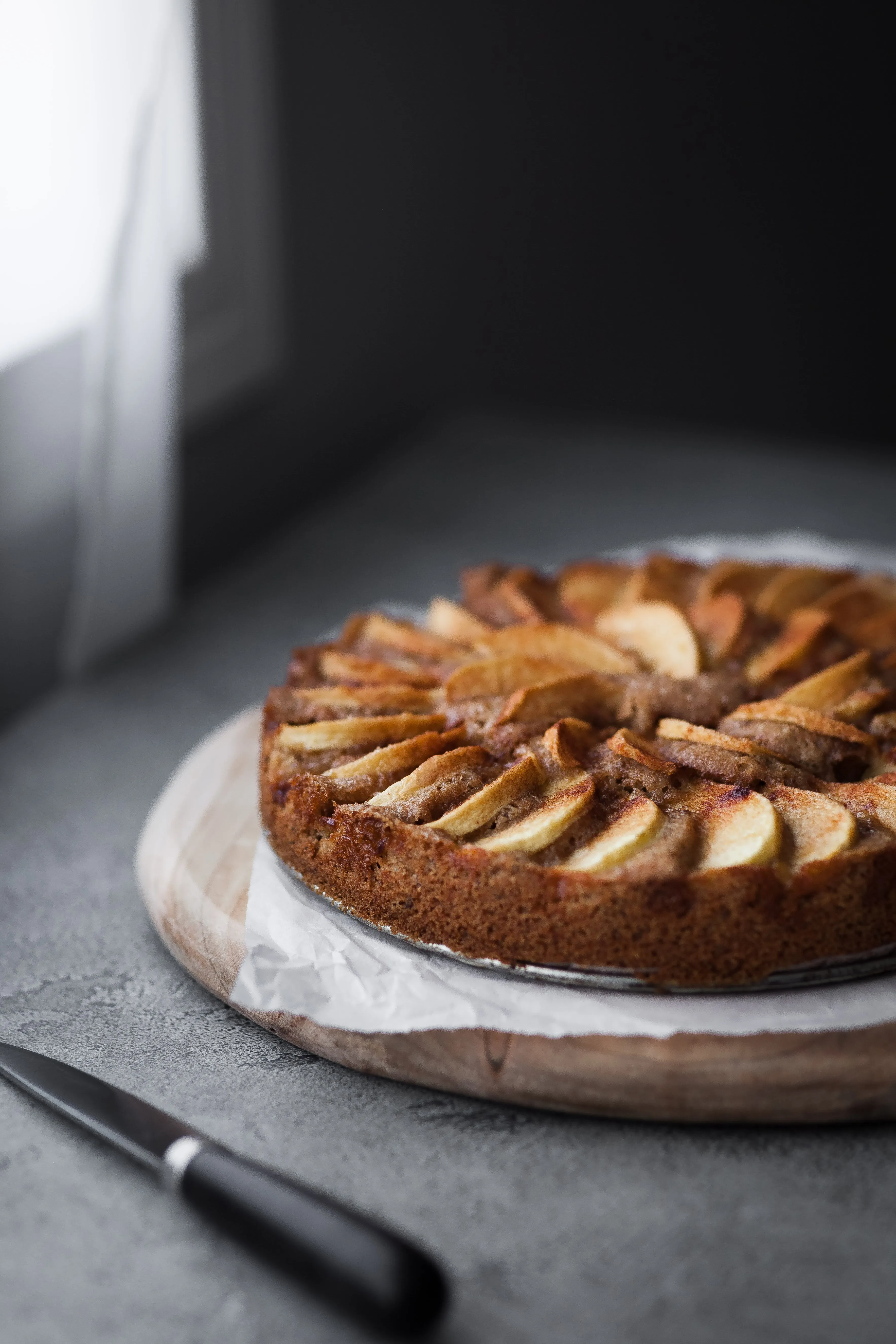 Ein angeschnittener deutscher Apfelkuchen in veganer Variante, auf einem Tisch am Fenster, bereit zum Servieren.