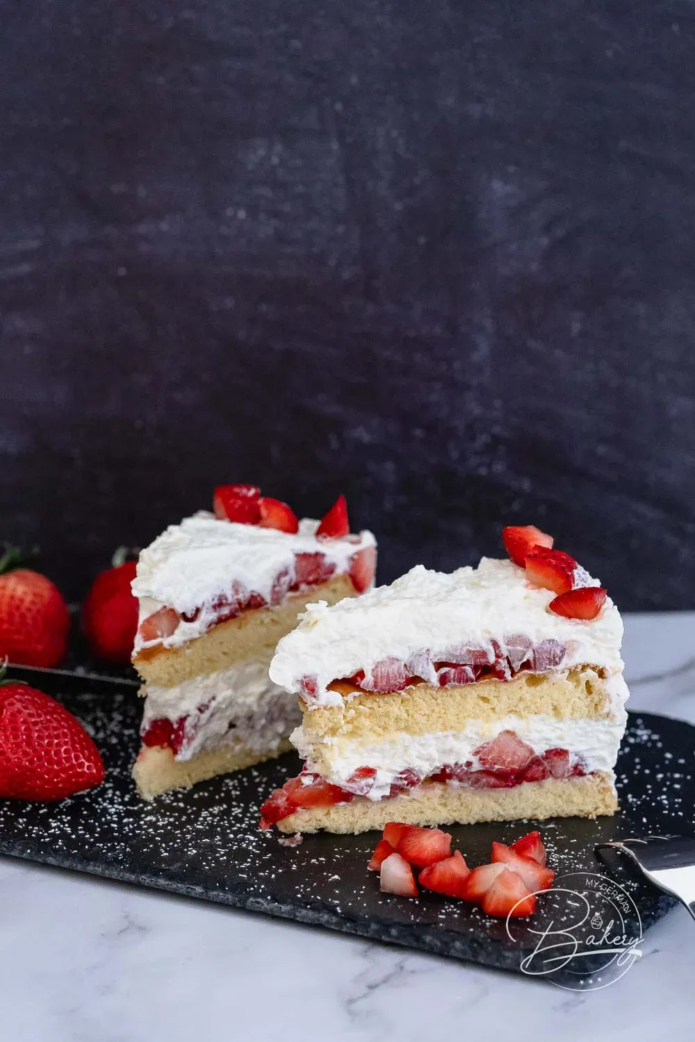 Ein angeschnittenes Stück der Erdbeer-Sahne-Torte zeigt die luftigen Biskuitböden, die reichhaltige Erdbeerfüllung und die leichte Sahneschicht.