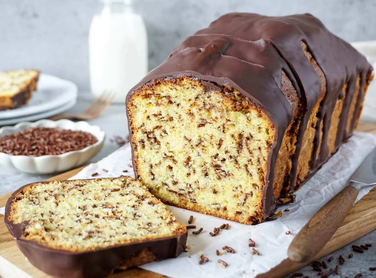 Ein appetitlich aussehender Kuchen, dekoriert mit frischen Beeren und Puderzucker, steht auf einem Holztisch.
