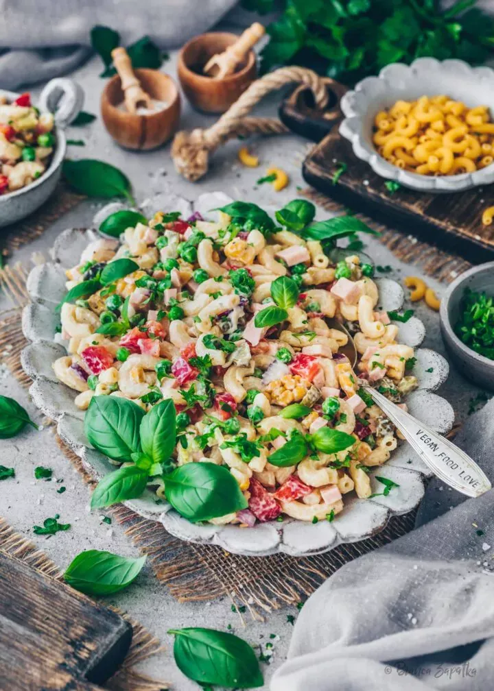 Ein Behälter mit cremigem veganen Nudelsalat, der vegane Fleischwurst, Gemüse und Dressing enthält und die einfache Aufbewahrung und Vorbereitung der Mahlzeit demonstriert.