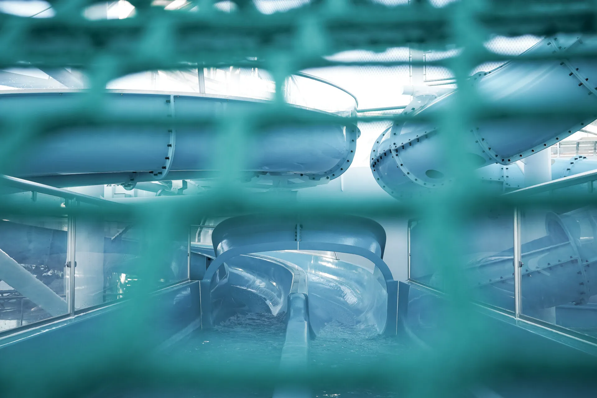 Ein Bild zeigt eine Wasserrutsche hinter einem Netz auf einem Kreuzfahrtschiff, das Meer im Hintergrund.