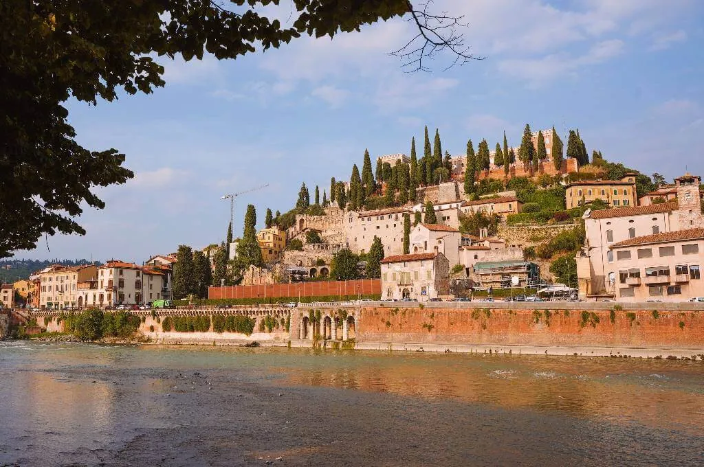 Ein Blick auf das Castel San Pietro in Verona vom Flussufer der Etsch. Das historische Schloss thront auf einem Hügel und bietet einen atemberaubenden Ausblick auf die Stadt.