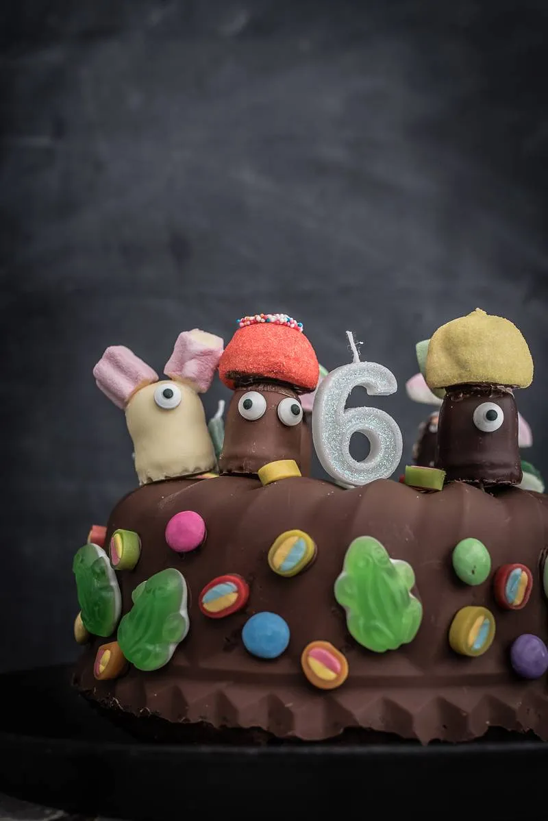 Ein bunter Kindergeburtstagskuchen, liebevoll mit Schokokuss-Gesichtern, Zuckeraugen und Schaumzuckerhüten dekoriert.