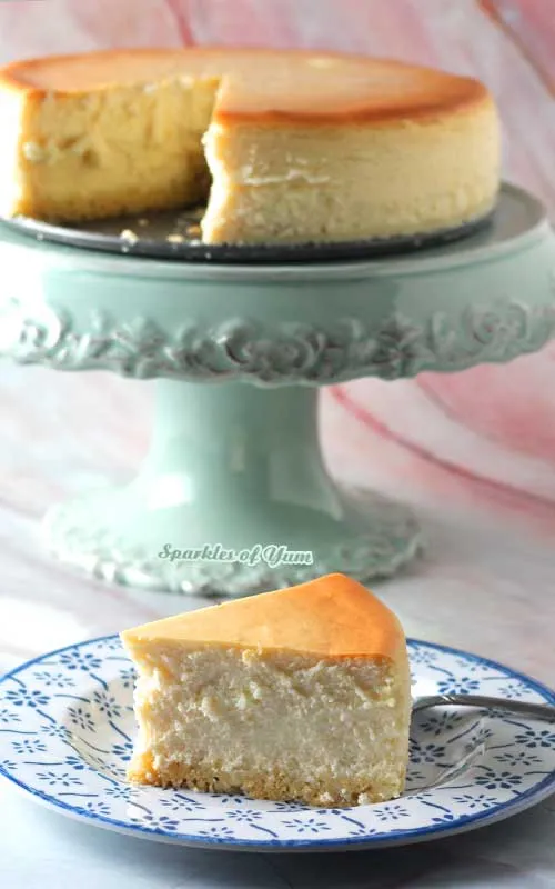 Ein cremiger New York Cheesecake, aus dem bereits ein Stück entnommen wurde, präsentiert auf einem Tortenständer.