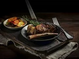 Ein deftiges Fleischgericht mit Beilagensalat, serviert auf dunklen Tellern und platziert über einem rustikalen Holzbrett.