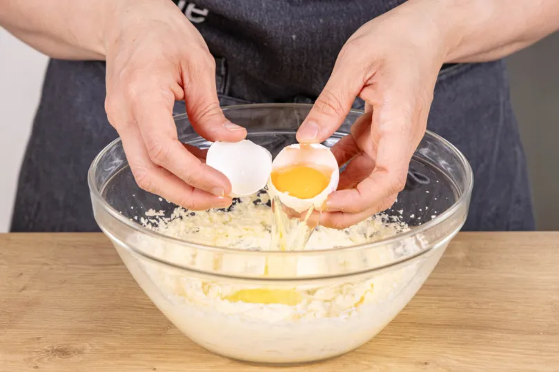 Ein Ei wird zum Teig für die Zitronen-Joghurt-Sahne-Torte hinzugefügt