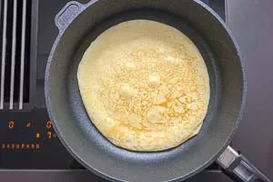 Ein Eierkuchen wird sorgfältig mit einem Pfannenwender in der Pfanne gewendet, um gleichmäßig zu bräunen.