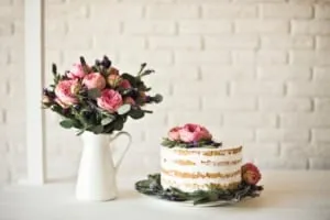 Ein einfacher Geburtstagskuchen, elegant dekoriert mit frischen Blumen und Beeren, auf einer rustikalen Holzplatte präsentiert, ideal für einen besonderen Anlass.