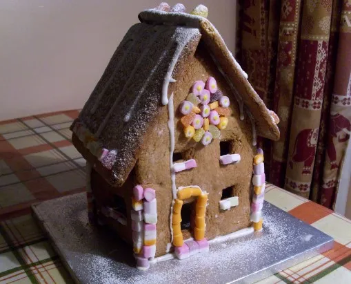 Ein fast fertig dekoriertes Lebkuchenhaus mit Eiszapfen aus Zuckerguss, bunten Süßigkeiten und einer Puderzuckerschicht.