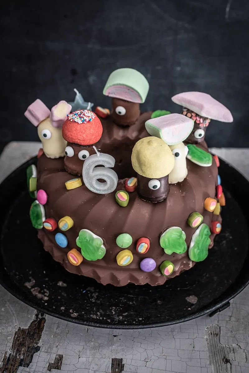 Ein fertig dekorierter, saftiger Marmorkuchen mit Schokokuss-Figuren und Süßigkeiten auf einer Etagere, bereit für den Kindergeburtstag.