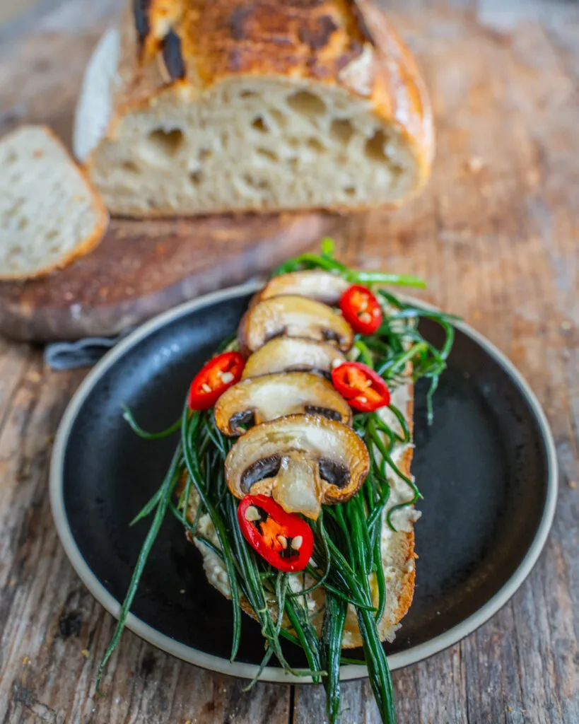 Ein fertiges Sauerteigbrot liegt auf einem Gitter zum Abkühlen bereit. Die Kruste ist goldbraun und knusprig.