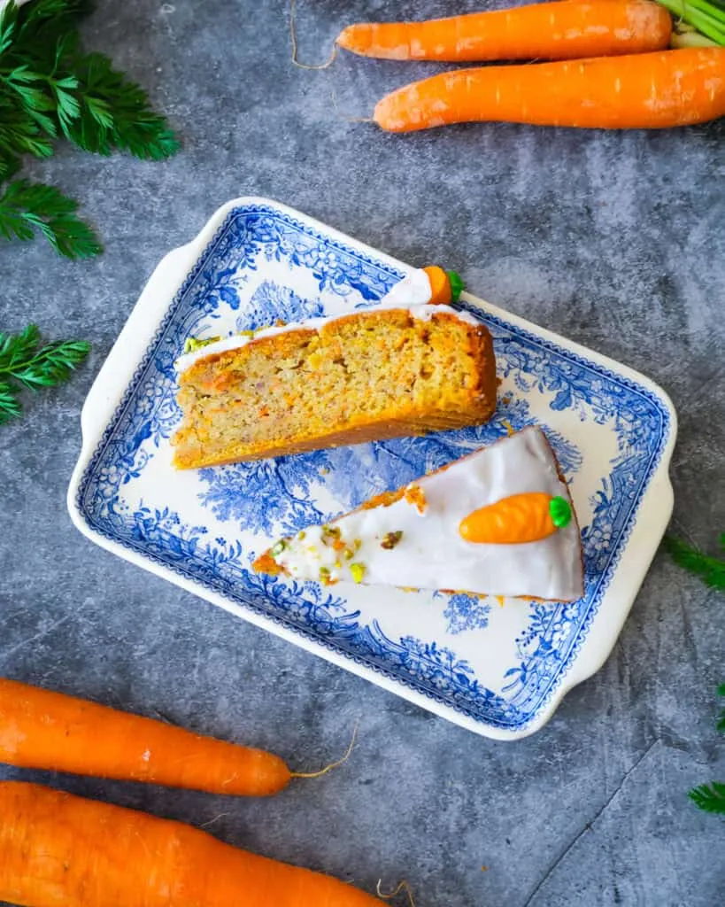 Ein frisch gebackener Rüblikuchen mit leuchtend grünen Marzipankarotten auf einer Holzplatte
