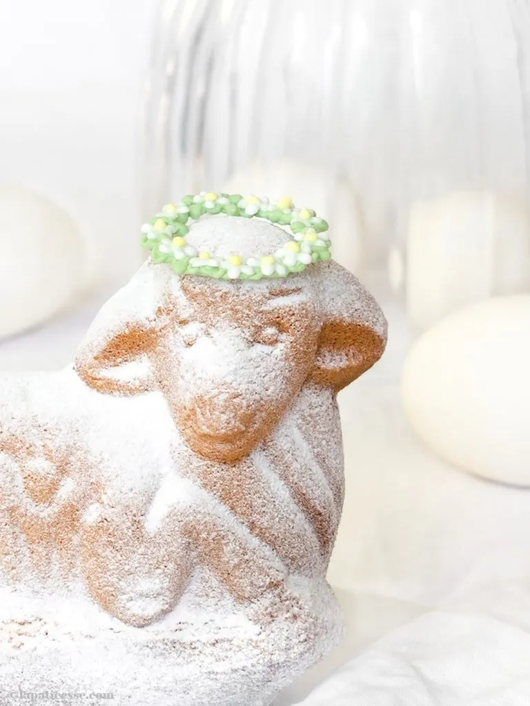 Ein frisch gebackenes, saftiges Osterlamm mit feinem Puderzucker und einem farbigen Blütenkranz als Dekoration.