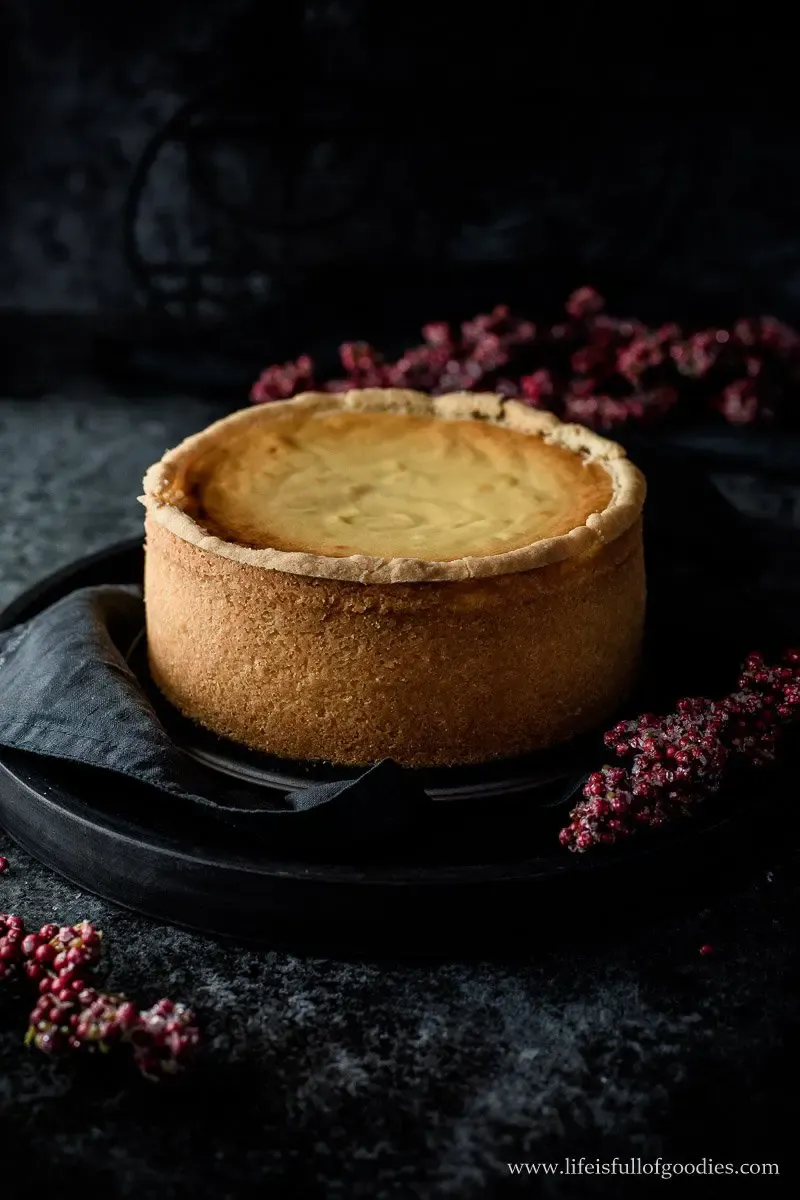 Ein ganzer, hoher Käsekuchen auf Holzbrett, bereit zum Servieren