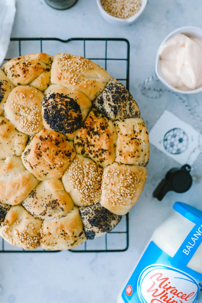 Ein gedeckter Tisch mit Grillgut, Salaten und einem Brötchenkranz im Mittelpunkt, der zu einem gemütlichen Beisammensein einlädt.