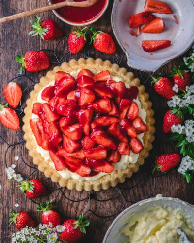 Ein glänzender, selbstgemachter Erdbeerguss wird vorsichtig über die frischen Erdbeeren auf der Torte gegossen, um die Erdbeer Pudding Sahne Torte zu vollenden.