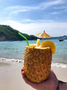 Ein Glas Piña Colada, garniert mit Ananas und Minze, vor tropischem Hintergrund