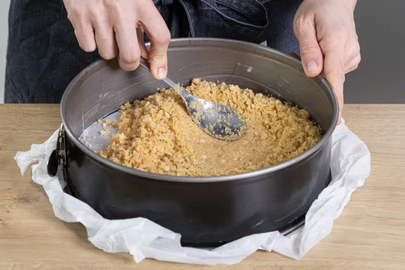 Ein gleichmäßiger Keksboden wird in eine Springform gedrückt, bereit für die Frischkäsecreme.