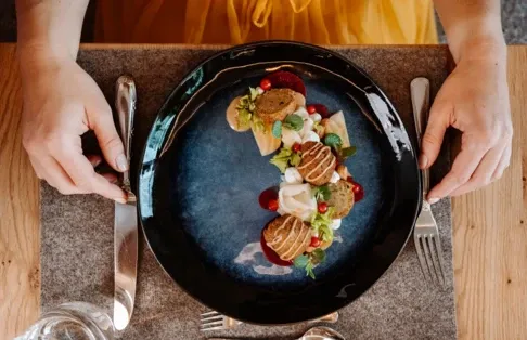 Ein Gourmet-Gericht, elegant präsentiert auf einem dunklen Teller, mit lebendigen Garnituren, auf einer Holztischdeko.