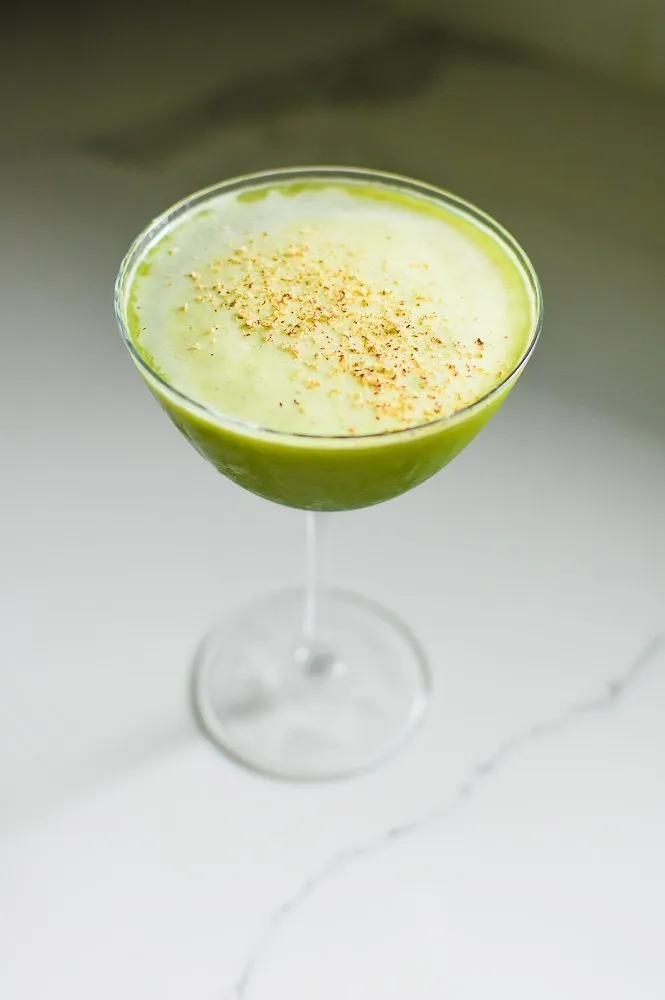Ein grüner Matcha-Martini in einem gekühlten Glas, garniert mit frisch geriebener Muskatnuss, auf einer Granitarbeitsplatte.