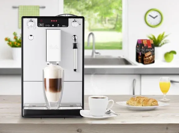 Ein Kaffeevollautomat mit Milchsystem bereitet einen Latte Macchiato zu, Teil eines gemütlichen Frühstücks in einem deutschen Haushalt.