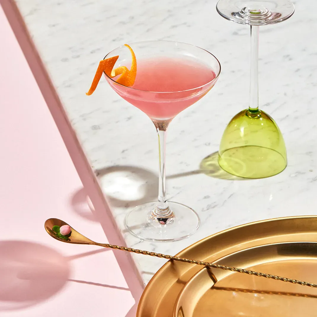 Ein klassischer Cosmopolitan Cocktail in einem Martiniglas mit Orangenzeste als Garnitur.